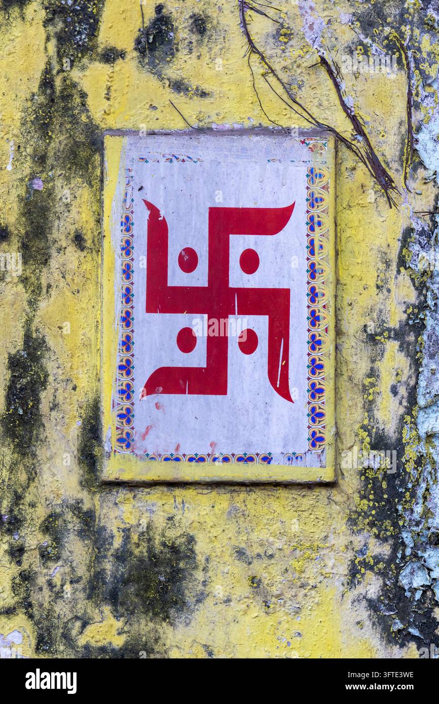 Swastika rossoindiana, simbolo sacro indù con punti in ogni quadrante su una piastrella su un muro giallo muschioso e screpolato, Bengala Occidentale, Kolkata, India Foto Stock