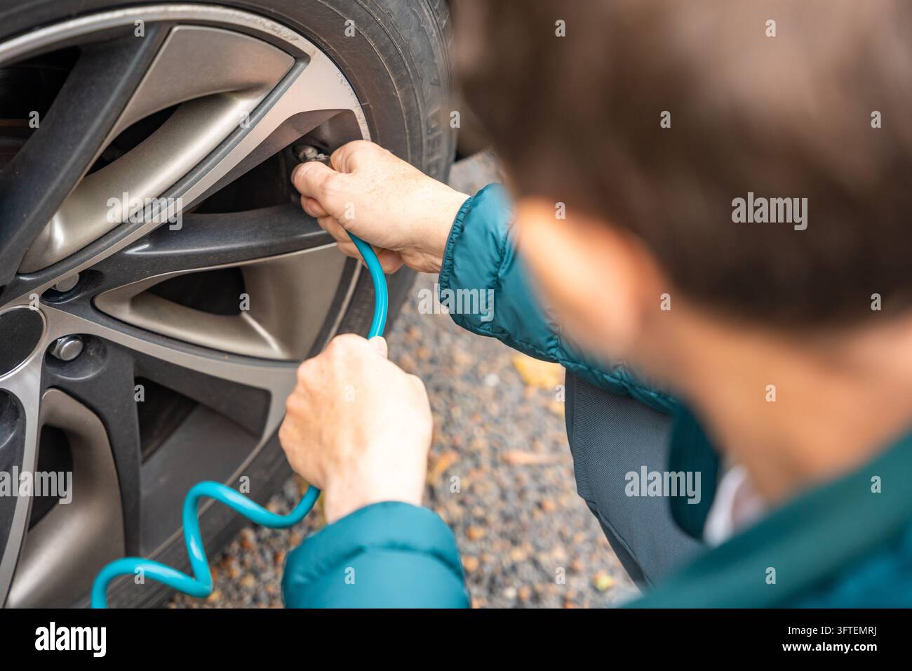 Un uomo collega un tubo dell'aria avvolto a una valvola dell'auto in una vista sopra la spalla. Il gonfiaggio regolare dei pneumatici aiuta a mantenere la pressione per la guida. Foto Stock