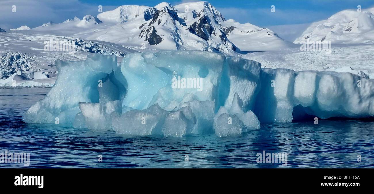 Grande iceberg blu scolpito che galleggia nelle acque antartiche, con montagne coperte di neve e ghiacciai sullo sfondo, Antartide. - Immagine stock catturata con smartphone