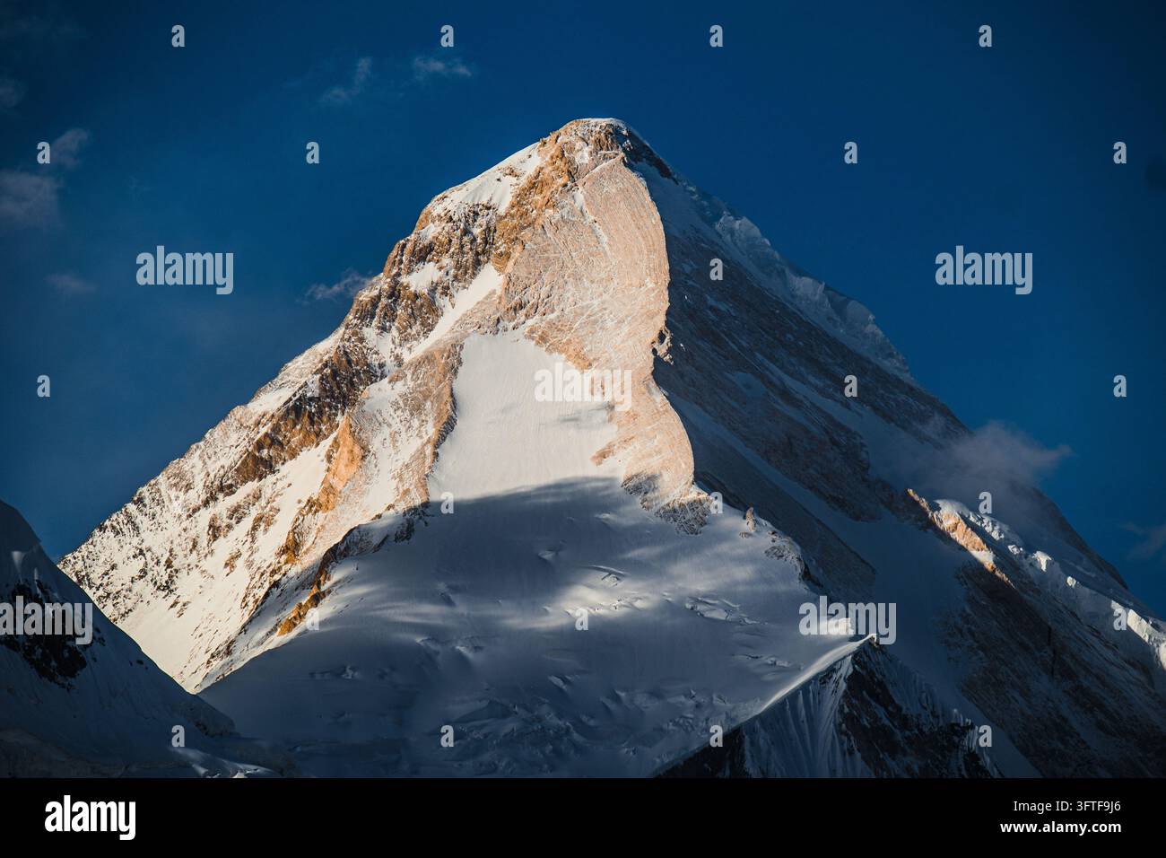 La luce del sole illumina la cresta montuosa ripida e triangolare coperta di neve e la parete verticale ghiacciata Foto Stock