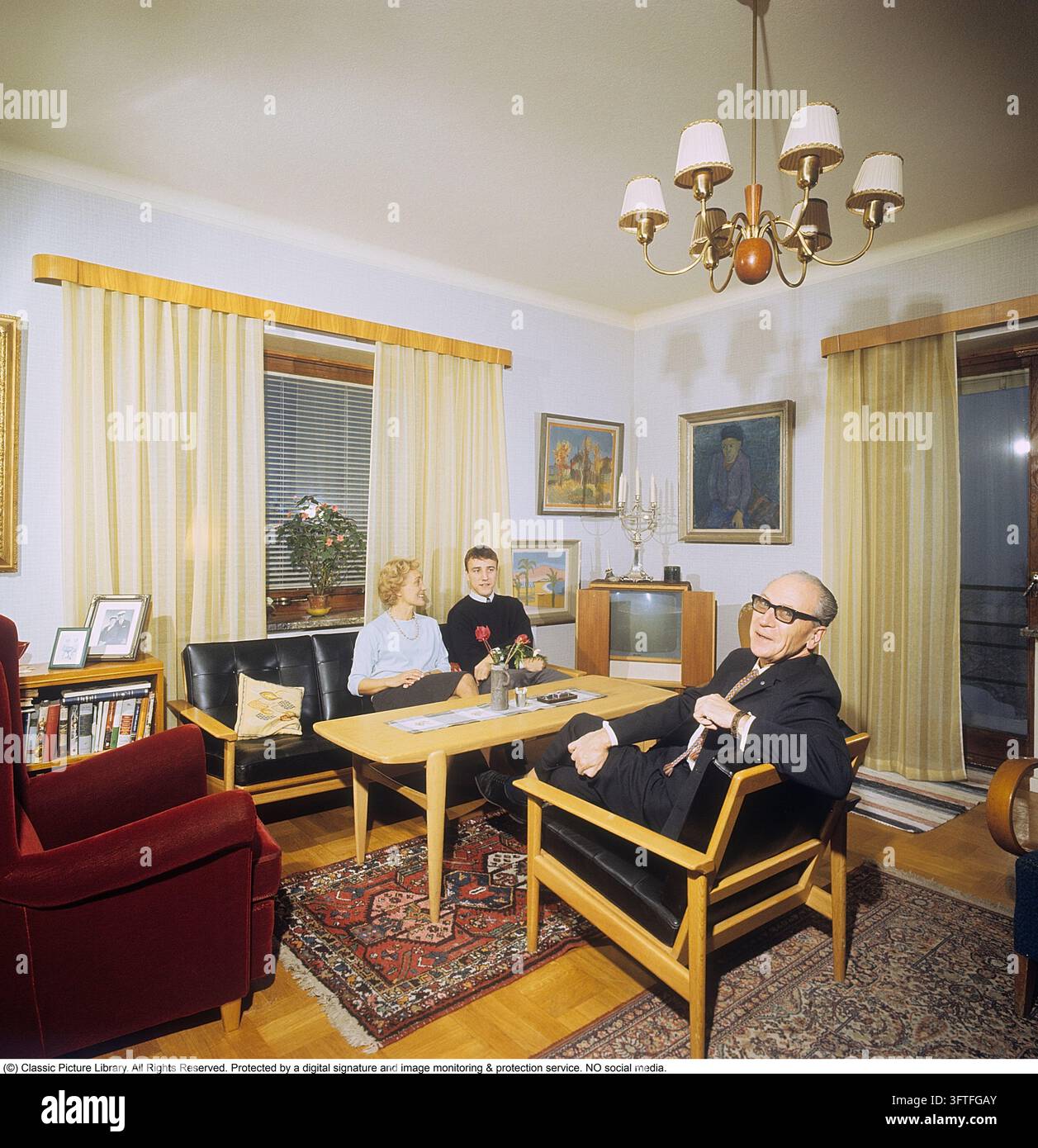 Una famiglia a casa alla fine degli anni '50. La televisione aveva iniziato con le sue prime trasmissioni e i primi televisori assomigliavano a quello che si trovava nell'angolo. Aveva pannelli pieghevoli che si chiudevano davanti allo schermo della tv quando non si guardava. I mobili e la decorazione interna sono del tipico stile degli anni '50 con sedie e divano con struttura in legno.    Anders Svahn ref SVA18 Foto Stock