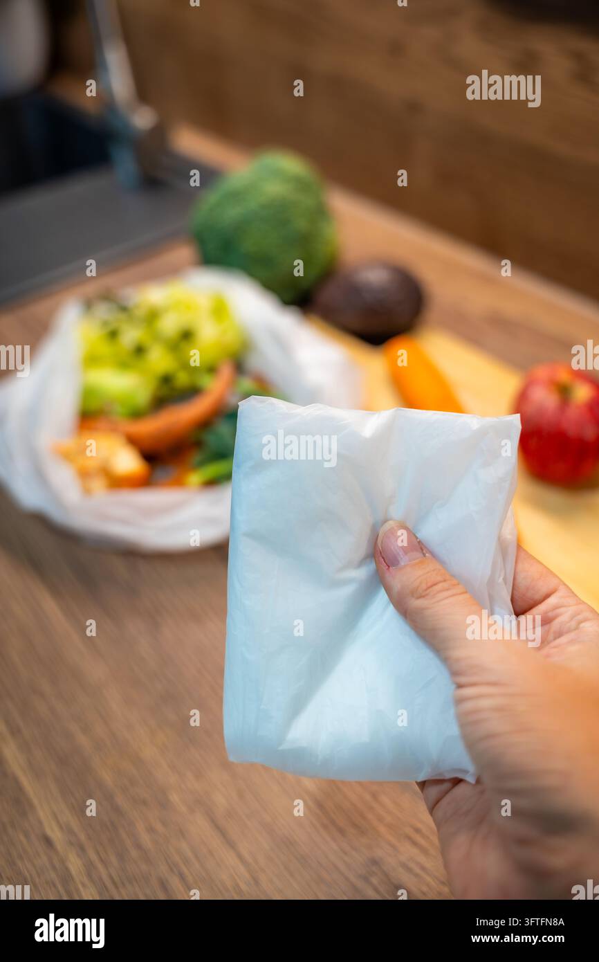 Una mano tiene sacchetti biodegradabili piegati con scarti di cibo sfocati sullo sfondo. Una pellicola biodegradabile sottile fornisce sacchetti per la raccolta dei rifiuti organici della cucina. Foto Stock