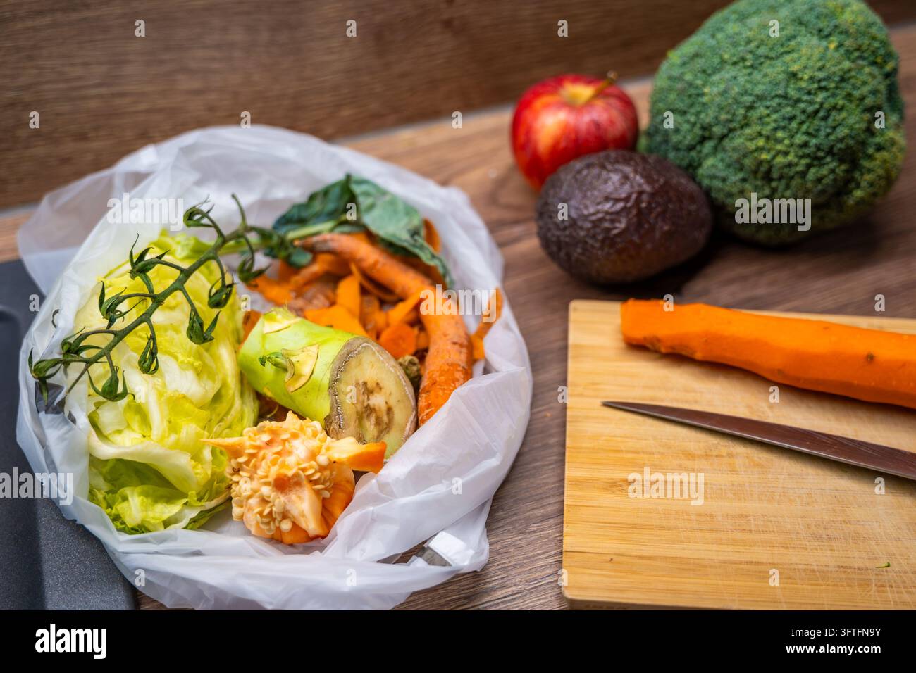 Un sac biodegradabile contiene scarti di verdure accanto a broccoli, una mela e un avocado. La raccolta separata dei rifiuti organici supporta il compostaggio domestico. Foto Stock
