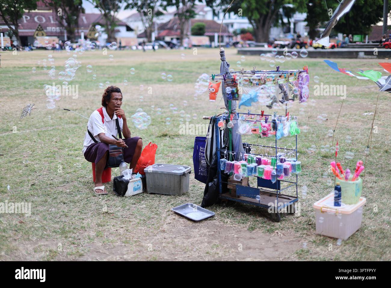 Un venditore ambulante è seduto accanto a un'esposizione mobile di giocattoli colorati, forniture per fare bolle di sapone e prodotti per bambini piccoli a Piazza Magelang (alun-alun). Foto Stock
