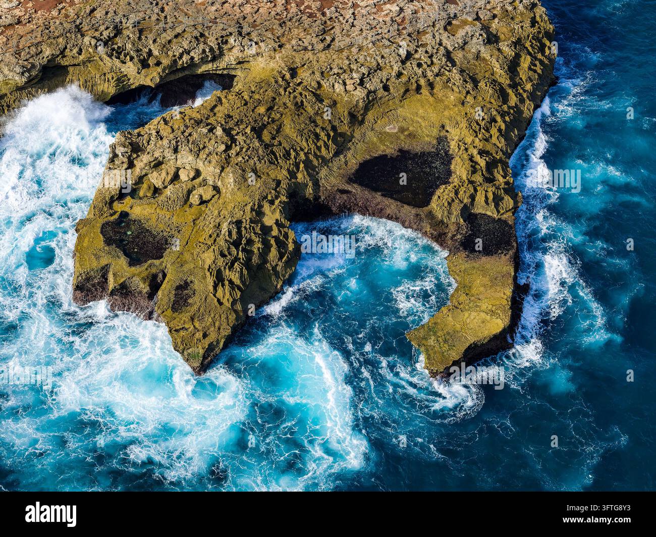 Veduta aerea del mare turchese che si infrange nelle insenature rocciose, onde che si infrangono contro scogliere texture e piscine di marea lungo la costa di un'isola tropicale Foto Stock