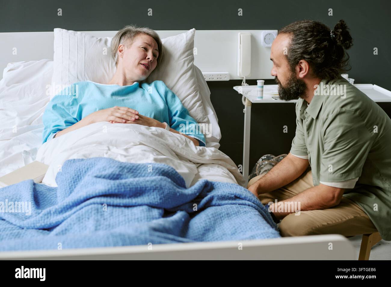 Uomo di mezza età in visita a una donna malata a riposo in un letto d'ospedale Foto Stock