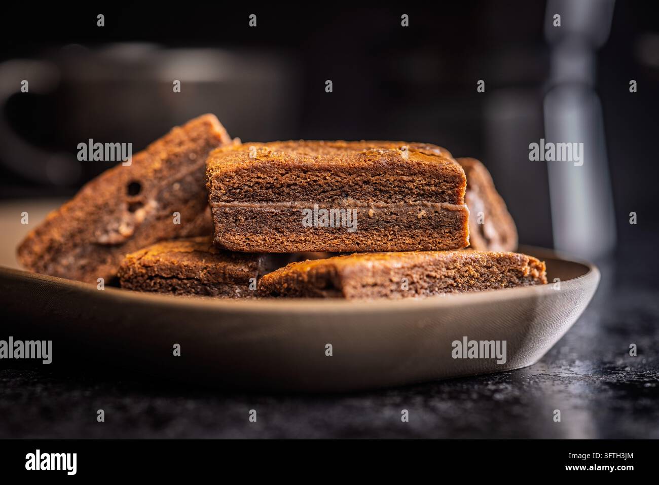 Brownies al cioccolato impilati su un piatto di ceramica che mostrano ricche strati di fudge e una morbida consistenza in un'illuminazione calda e suggestiva, perfetti per panetteria, caffè, dessert, Foto Stock