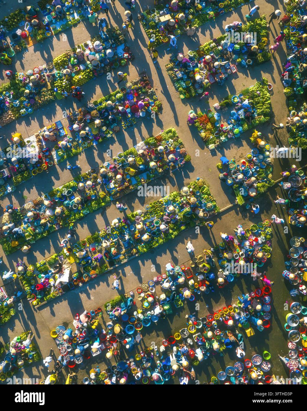 Vista aerea del mercato di Vi Thanh con bancarelle colorate, venditori con cappelli a cono e prodotti freschi disposti in file ordinate sotto la calda luce del mattino Foto Stock