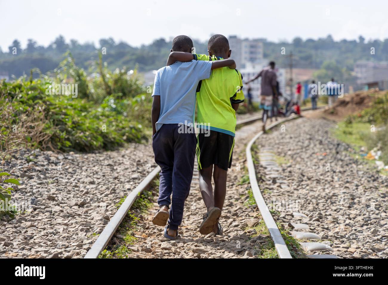 Due ragazzi che camminano braccio sopra spalla lungo i binari ferroviari nell'area di Kibera, Contea di Nairobi, Nairobi, Kenya Foto Stock
