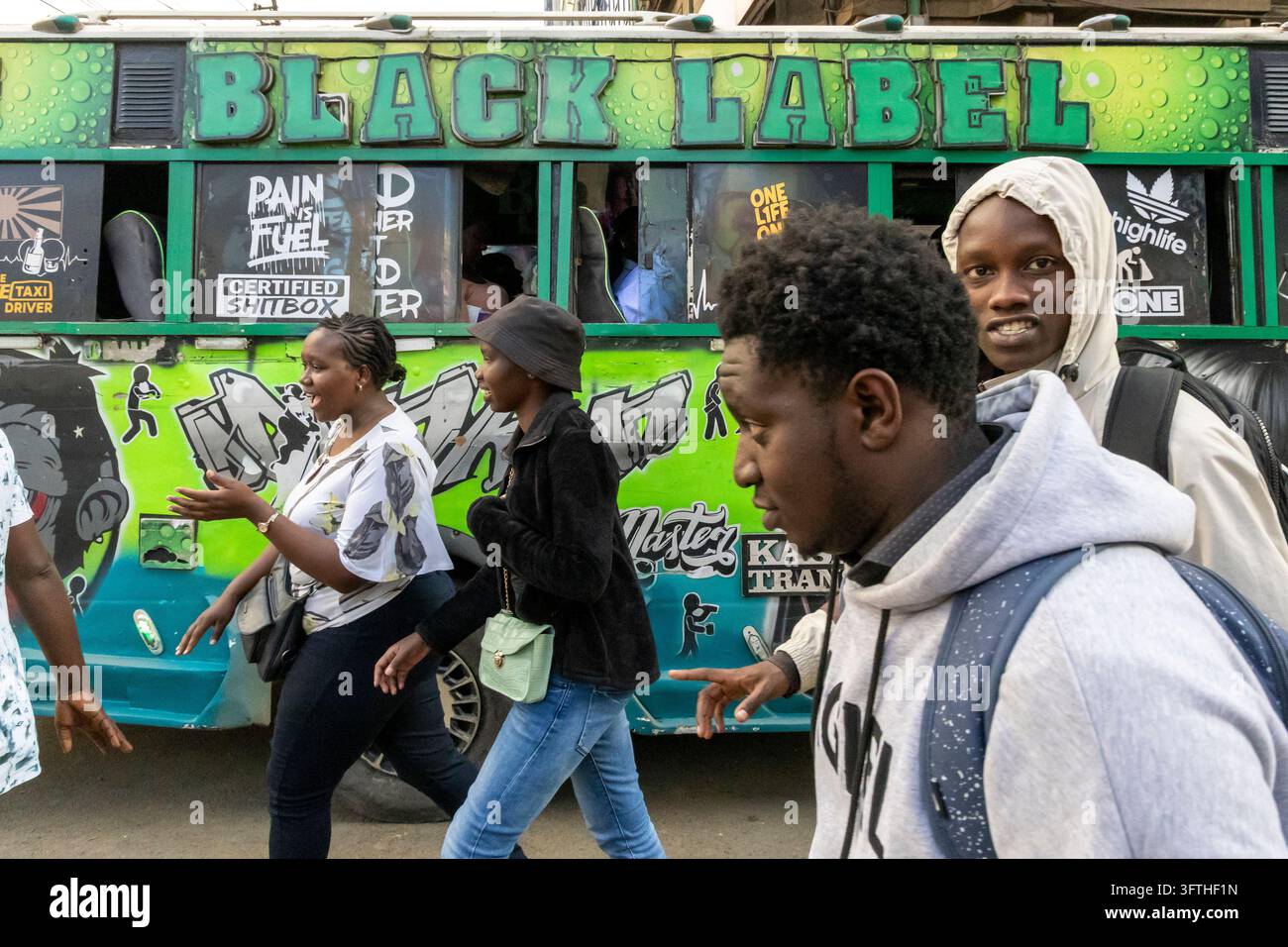 Giovani uomini e donne che passano davanti a un minibus matatu verde con scritte e adesivi Black Label, Contea di Nairobi, Nairobi, Kenya Foto Stock