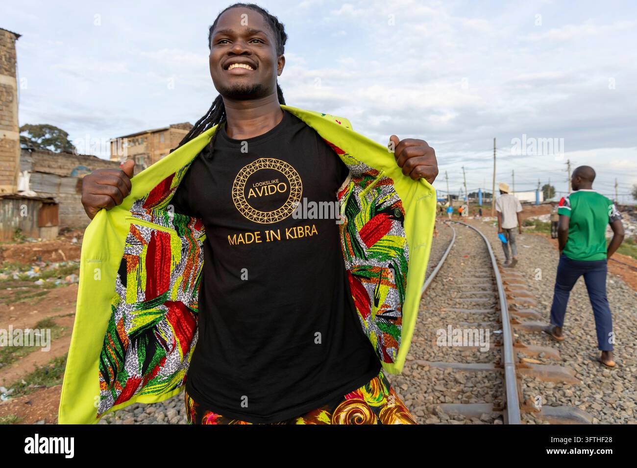David Avido, stilista, apre un blazer verde lime per mostrare una maglietta Made in Kibra su una ferrovia, Contea di Nairobi, Nairobi, Kenya Foto Stock
