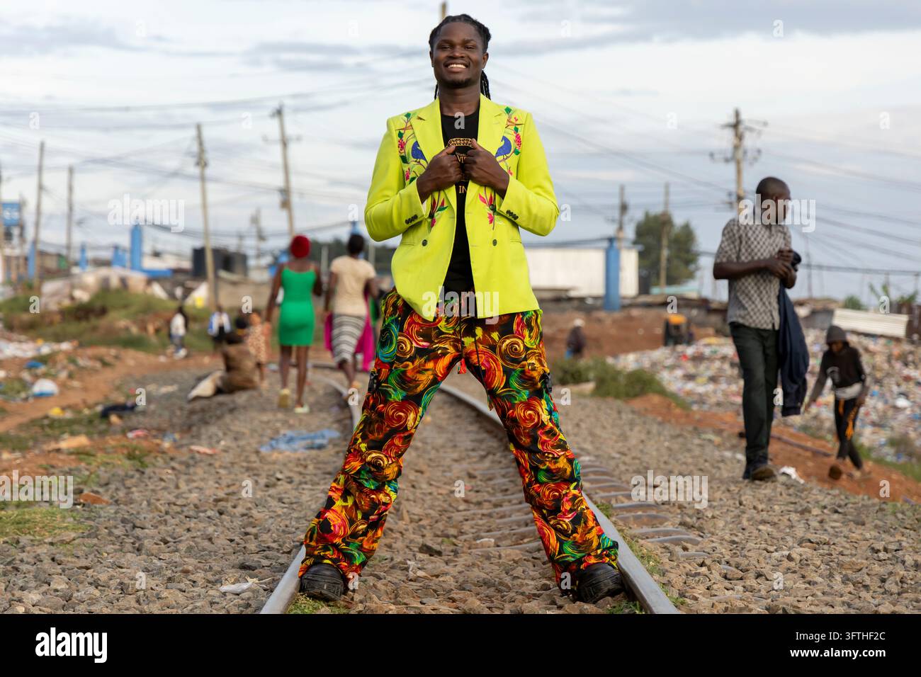 David Avido stilista in un blazer verde lime e pantaloni con stampa a vortice, seduto su una linea ferroviaria, Contea di Nairobi, Nairobi, Kenya Foto Stock