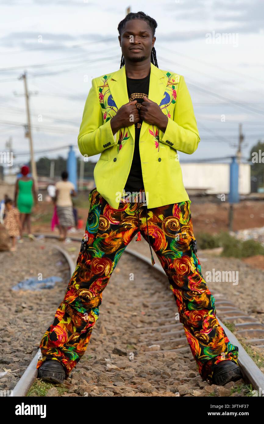 David Avido stilista in un blazer verde lime e pantaloni con stampa a vortice su una ferrovia a Kibera, Contea di Nairobi, Nairobi, Kenya Foto Stock