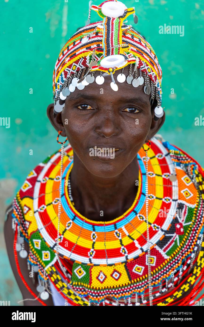 Donna della tribù Rendille con un copricapo ricoperto di perle e un grande collare a strati di perle davanti a un muro verde, Contea di Marsabit, Loiyangalani, Kenya Foto Stock