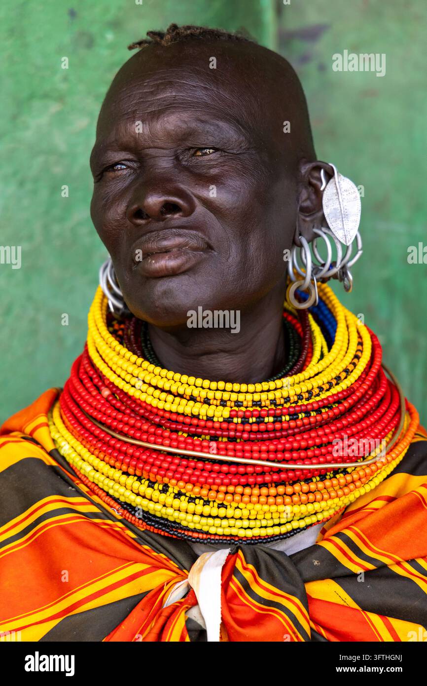 Donna anziana con collane a strati di perle e orecchini d'argento vicino a un muro verde al Festival del Lago Turkana, Contea di Marsabit, Loiyangalani, Kenya Foto Stock