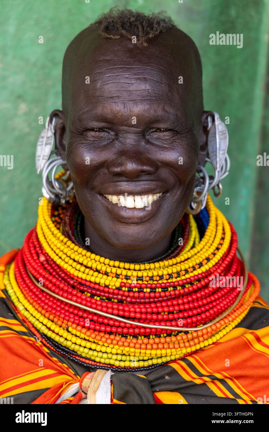 Donna sorridente della tribù Turkana con collane a strati di perle e grandi orecchini d'argento davanti a un muro verde, Contea di Marsabit, Loiyangalani, Kenya Foto Stock