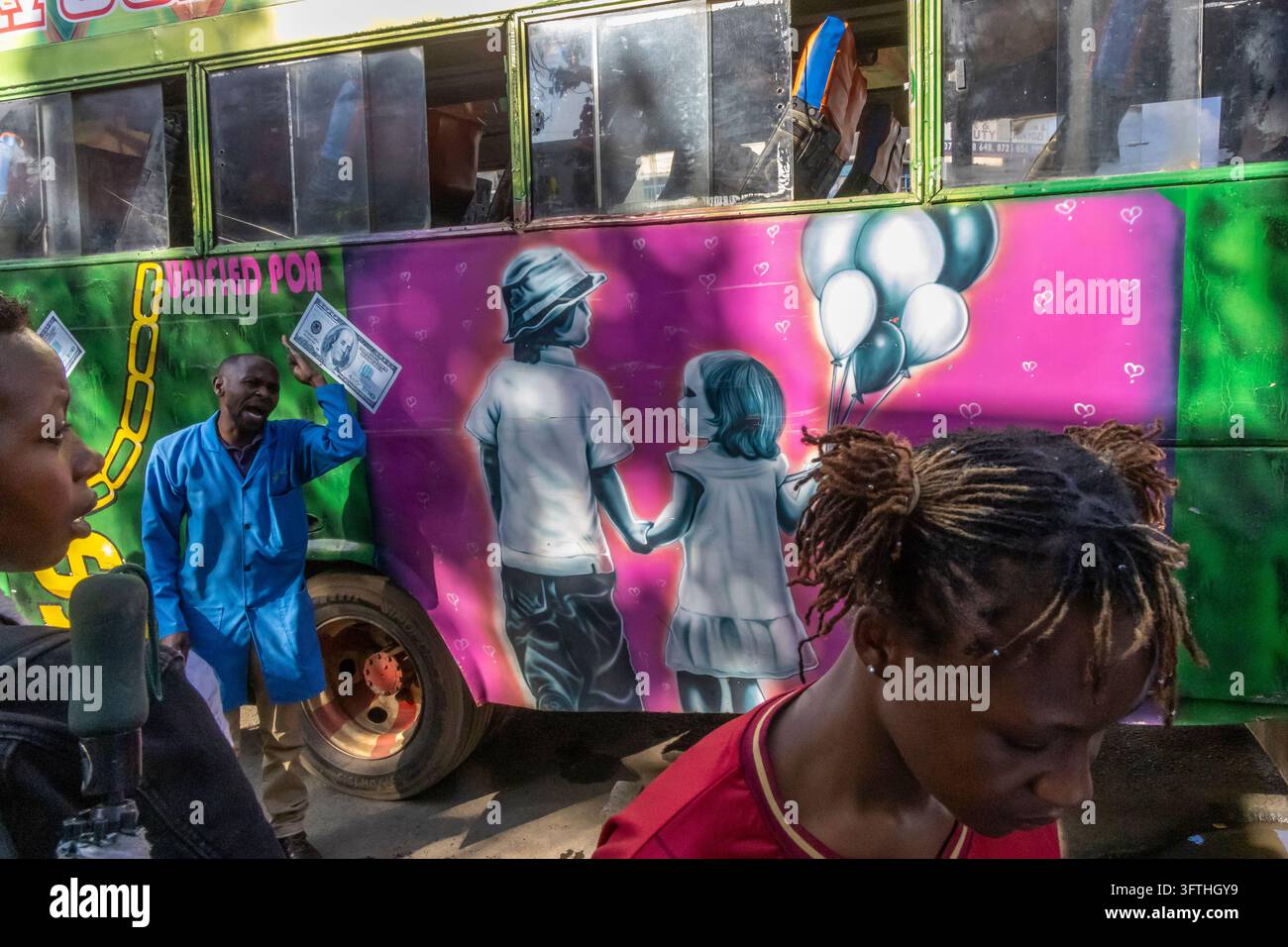 Uomo in cappotto blu che tiene un falso biglietto da un dollaro accanto a una matatu verde dipinta con bambini e palloncini, Contea di Nairobi, Nairobi, Kenya Foto Stock