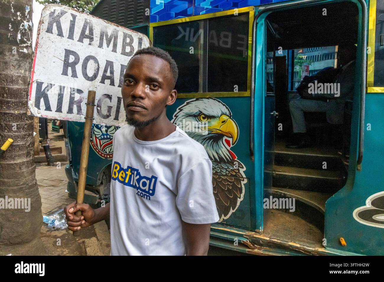 Giovane uomo che tiene un cartello Kiambu Road Kirigiti accanto a un minibus matatu verde dipinto con un'illustrazione di un'aquila, Contea di Nairobi, Nairobi, Kenya Foto Stock