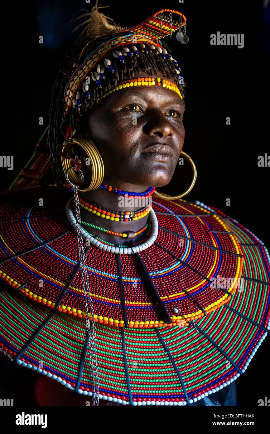 Donna della tribù Pokot su sfondo nero con copricapo di piume e ampio collare di perle rosse e verdi, Contea di Baringo, Churo, Kenya Foto Stock