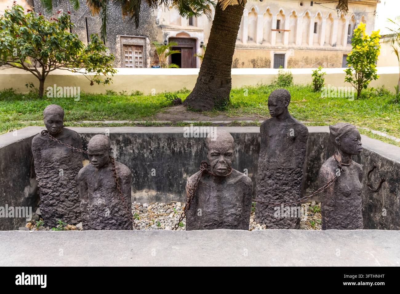 Memoriale della mostra sul commercio di schiavi dell'Africa orientale con cinque figure scolpite incatenate da collari di ferro in una fossa di pietra, Stone Town, Tanzania Foto Stock