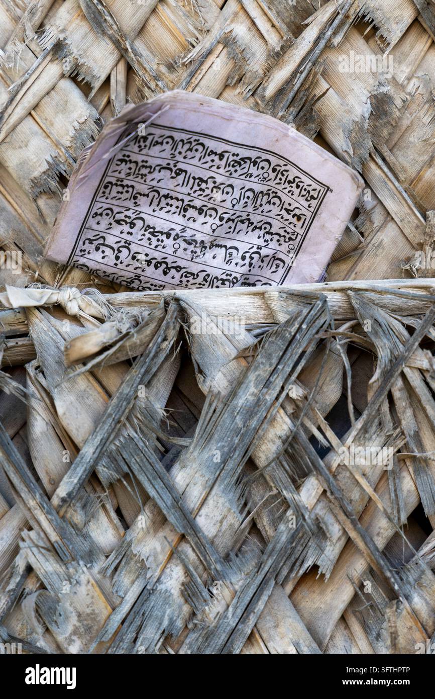 Vecchio opuscolo consumato con scrittura araba infilato in un muro di foglie di palma tessute e consumate con strisce grigie e beige sfilacciate, Matemwe, Tanzania Foto Stock