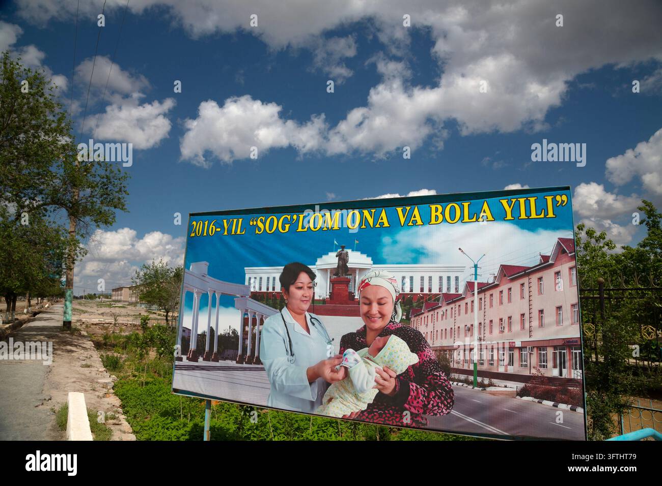 Cartellone stradale di un medico sorridente e di una madre che tiene un bambino davanti a grandi edifici sotto un cielo azzurro con nuvole, Moynaq, Uzbekistan Foto Stock