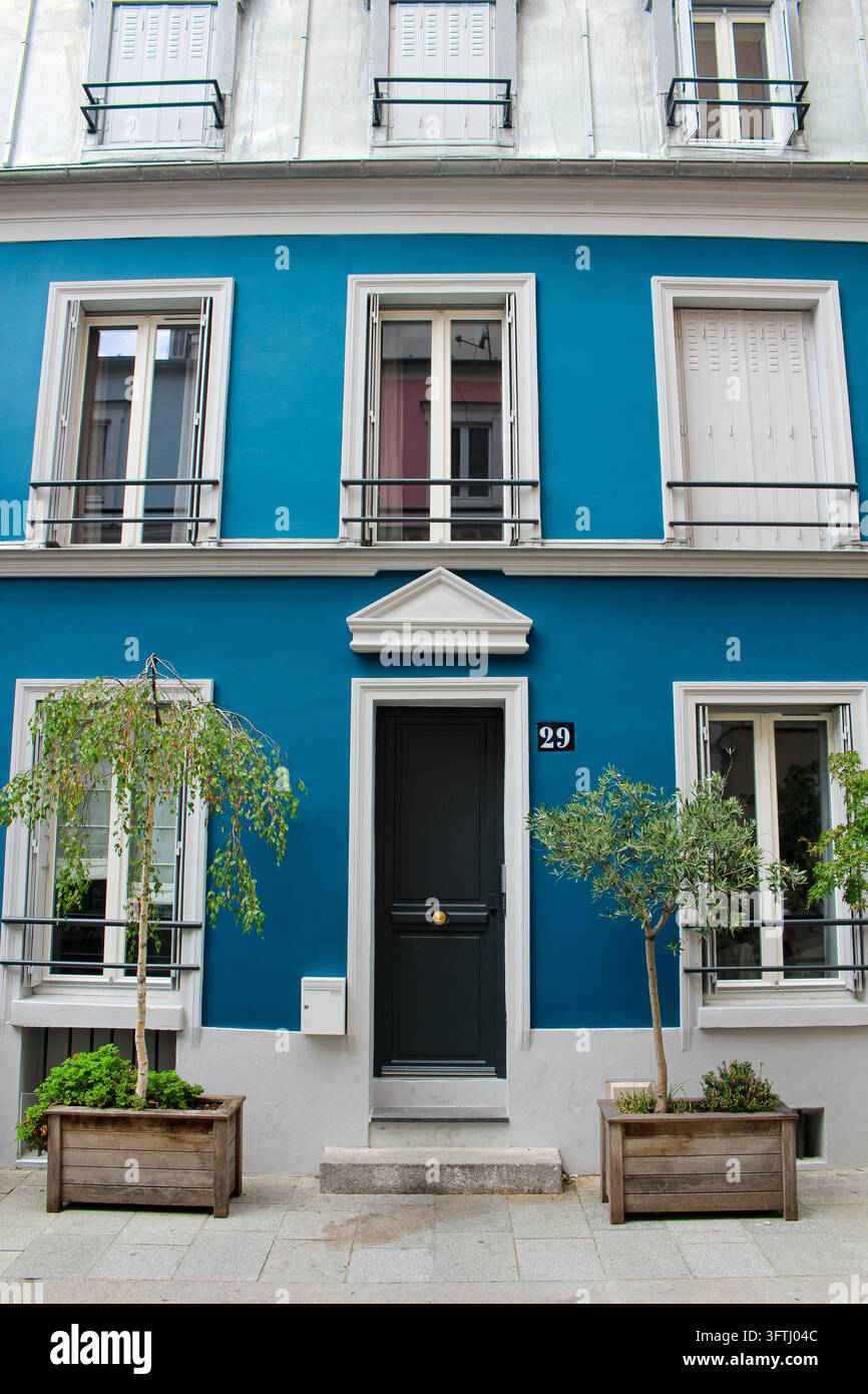 Parigi, Francia - 31 luglio 2019: Vista di una facciata di edificio blu vivace con una porta d'ingresso scura numerata 29 e due piccoli alberi in vasi di legno. Foto Stock