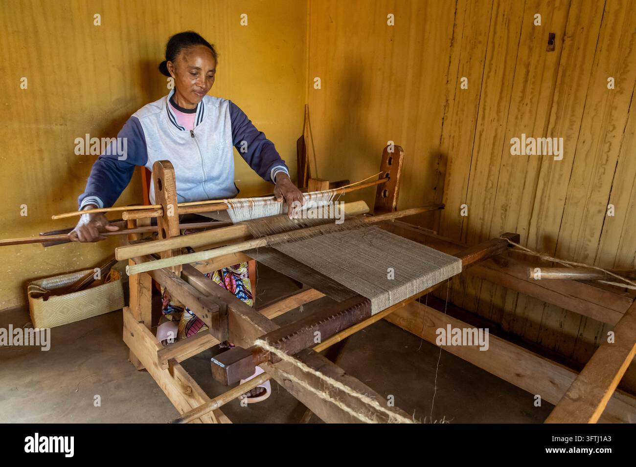 Una donna aziona il navetta di legno e il battitore di un telaio tradizionale mentre tesse stoffa, Haute Matsiatra, Ambalavao, Madagascar Foto Stock
