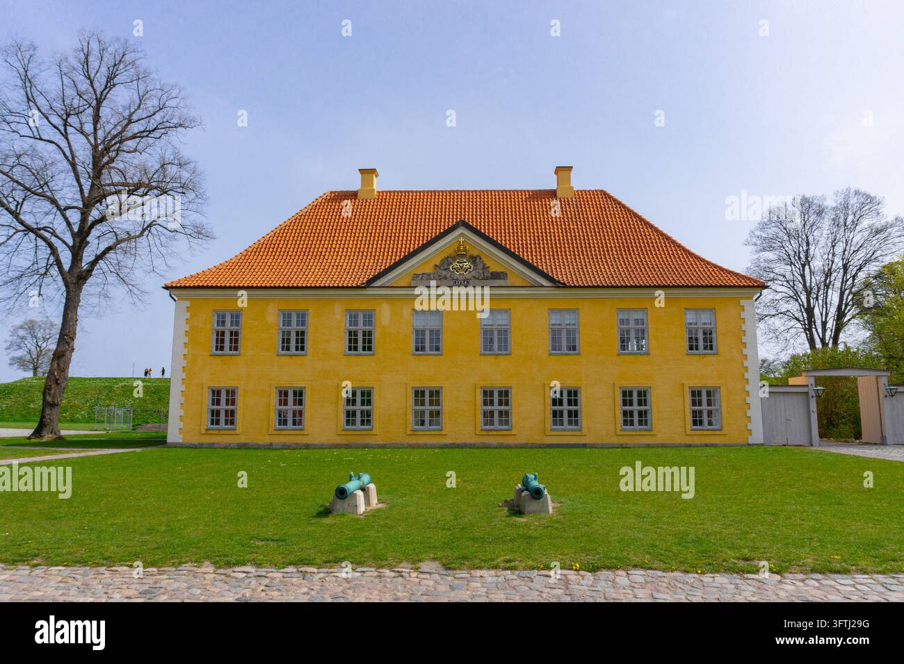 Copenaghen, Danimarca - 22 aprile 2019: Vista dell'edificio storico giallo di Kastellet con tetto di tegole arancioni, prato verde e due vecchi cannoni nel Foto Stock