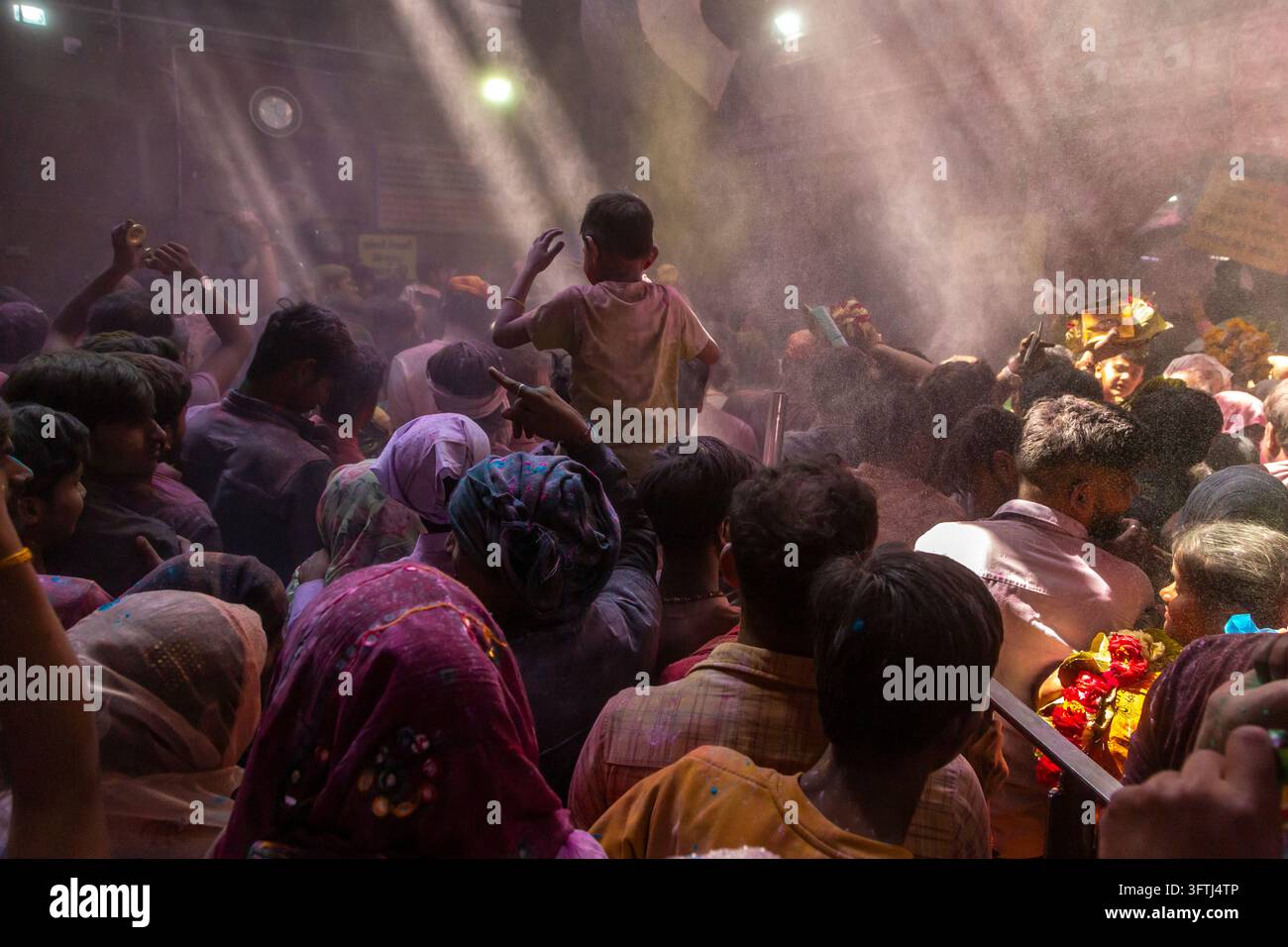 Bambino sollevato sopra una folla fitta all'interno del tempio Shri Banke Bihari mentre raggi di luce tagliano nuvole di polvere, Uttar Pradesh, Vrindavan, India Foto Stock