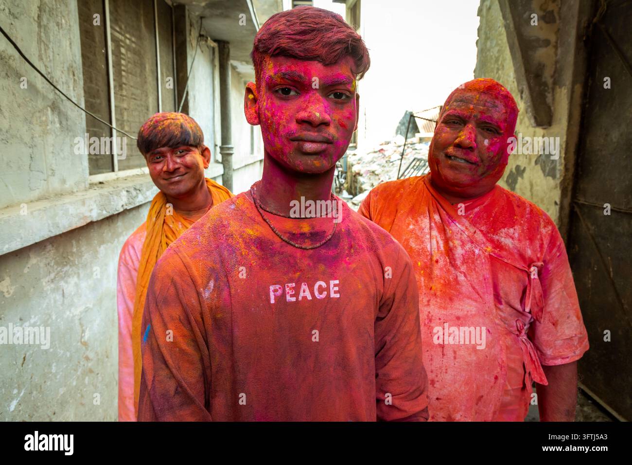 Tre uomini sorridenti con gulal rosa e arancione sul viso e sui vestiti posano insieme, Uttar Pradesh, Vrindavan, India Foto Stock