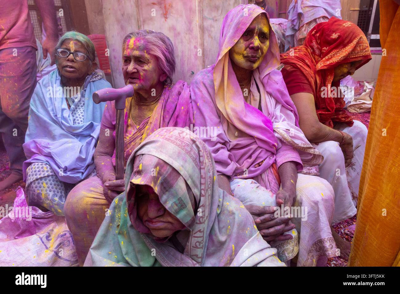 Donne anziane sedute fianco a fianco in sari colorati con gulal viola e giallo sul viso, una dell'Uttar Pradesh, Vrindavan, India Foto Stock