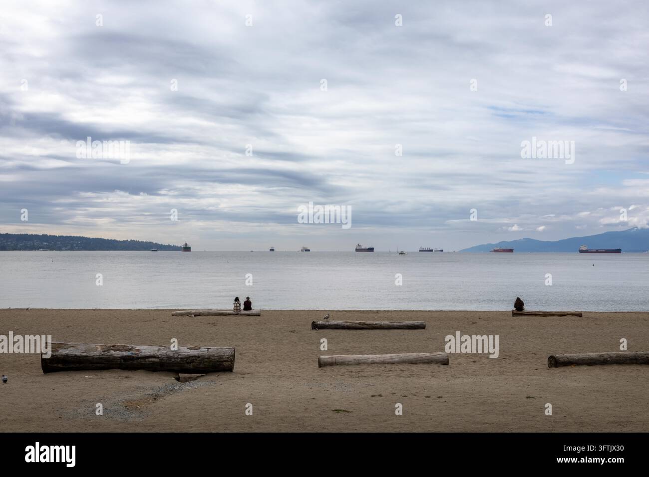 Vancouver, Canada – 7 settembre 2026: Scatto grandangolare orizzontale lungo la spiaggia sabbiosa di English Bay e tronchi alla deriva sparsi verso le acque aperte del mare d Foto Stock