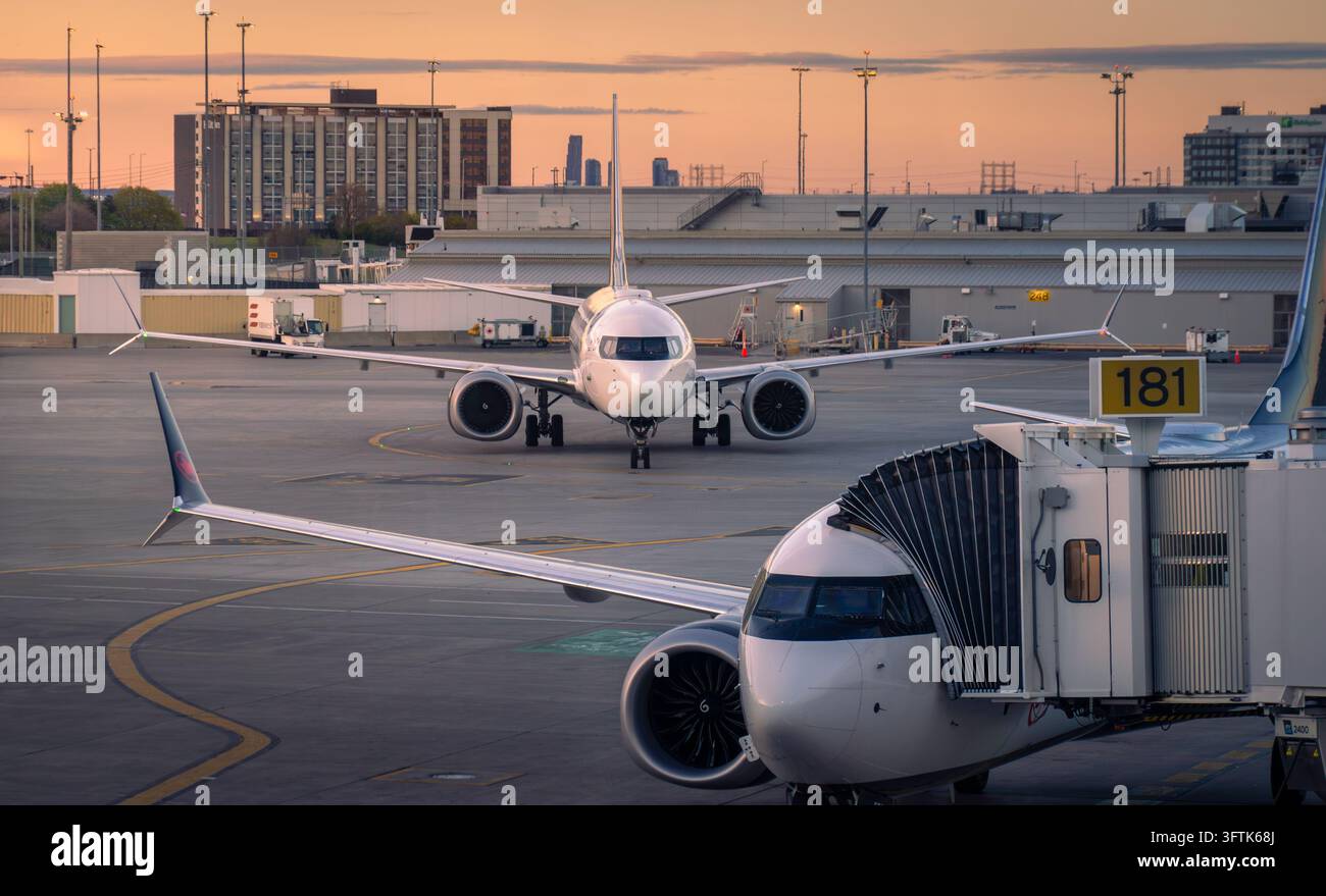 Toronto, Ontario, Canada - 05 26 2026: Aerei passeggeri commerciali ormeggiate al gate del terminal aeroportuale sul piazzale di servizio collegate a una passerella durante il tramonto Foto Stock