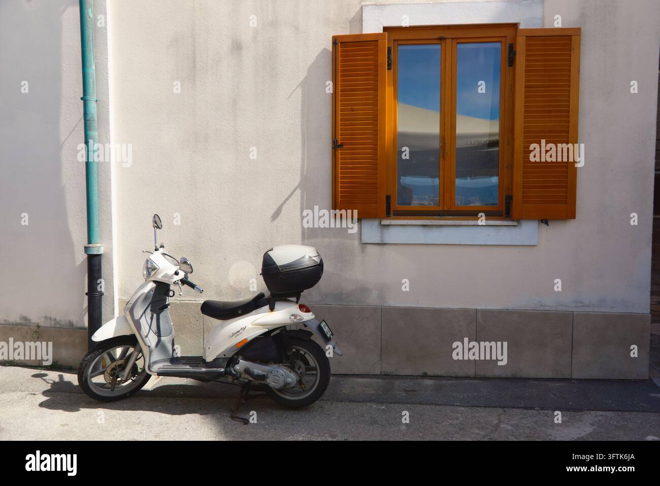 Scooter bianco parcheggiato fuori da una casa mediterranea tradizionale con persiane in legno in un vicolo tranquillo di Pirano, Slovenia. Foto Stock