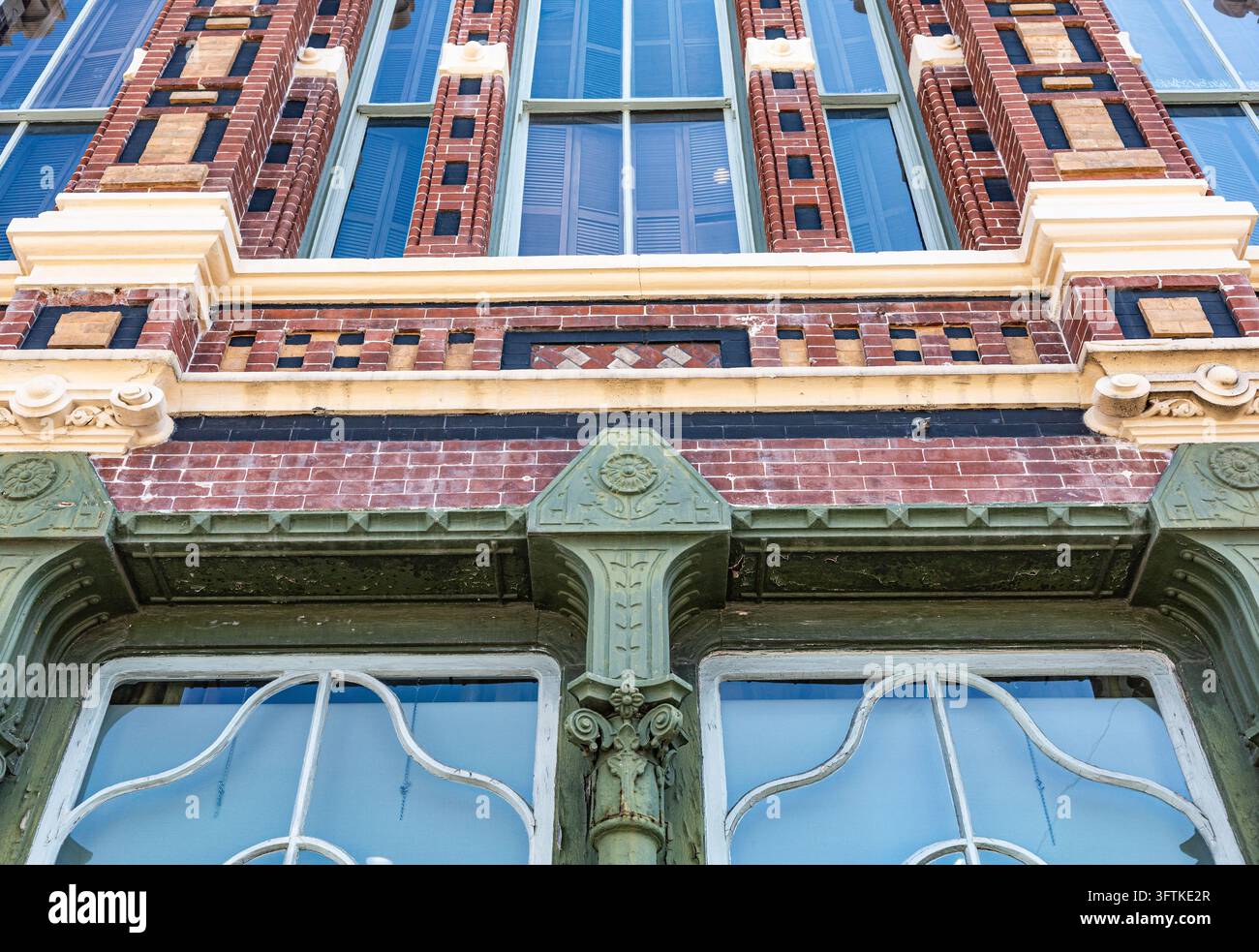 Primo piano di una facciata di edificio storico con muratura decorativa in mattoni rossi, supporti architettonici verdi ornati, finiture color crema e distin Foto Stock