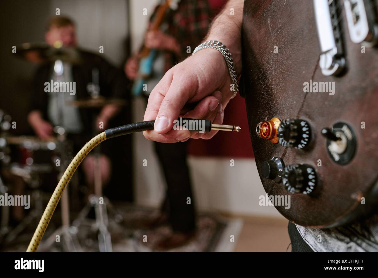 Musicista che inserisce un cavo audio in una chitarra elettrica durante la prova della band Foto Stock