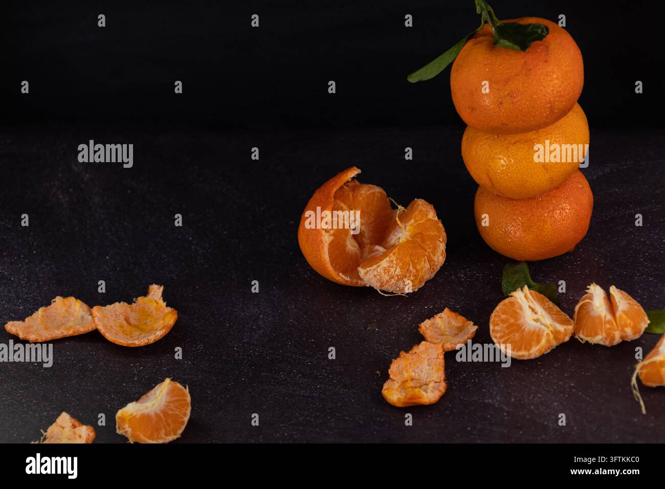 Mandarini freschi impilati su uno sfondo rustico con mandarini pelati sparsi intorno. Cibo scuro Foto Stock