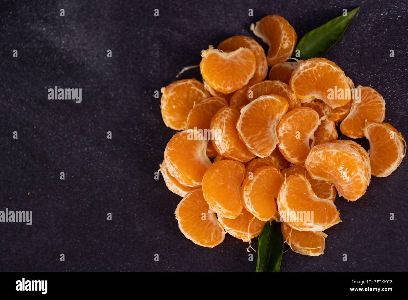 Vista dall'alto di segmenti di mandarini ammucchiati su uno sfondo rustico. Cibo scuro di mandarini Foto Stock