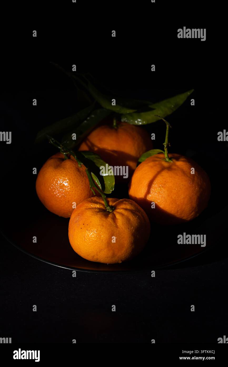 Immagine verticale di mandarini su un piatto nero su uno sfondo scuro con spazio per il testo. Frutta sana ricca di vitamina C Foto Stock