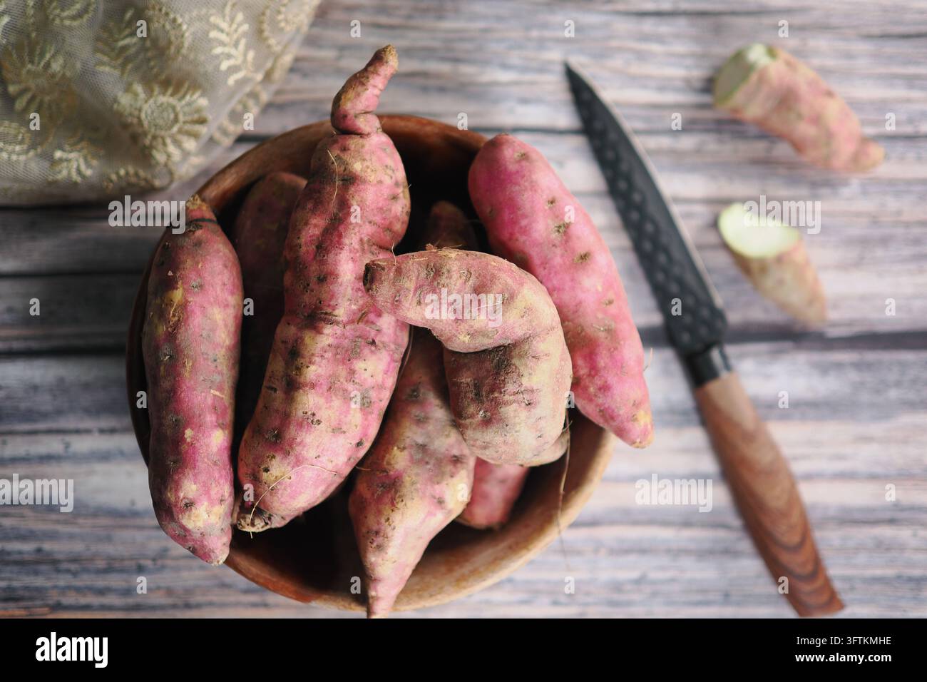 Patate dolci in una ciotola di legno su un tavolo di legno con un coltello nelle vicinanze Foto Stock
