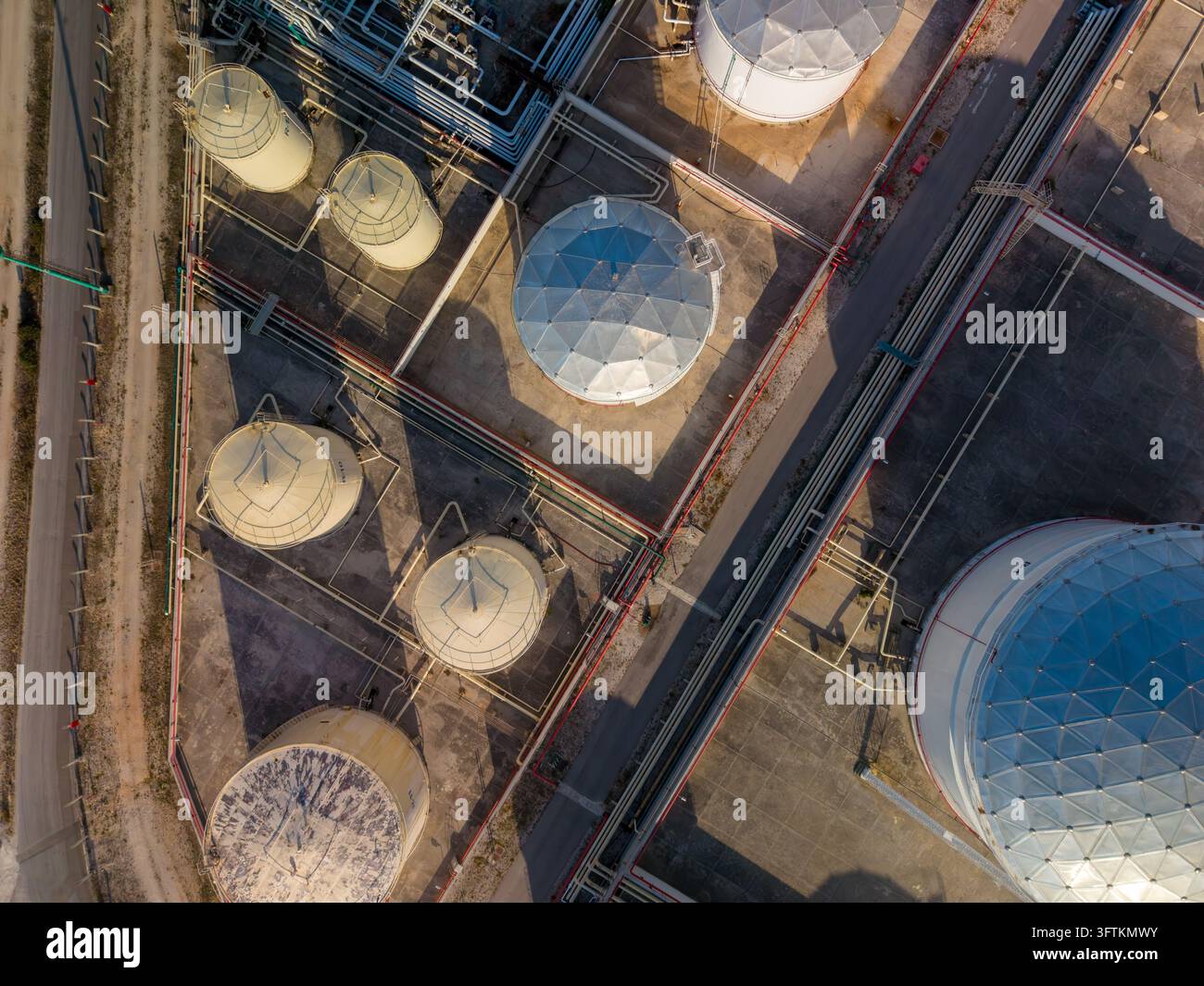 Vista aerea di serbatoi di stoccaggio, supporti per tubi e corsie di servizio in un impianto industriale. Vasche rotonde e tubazioni interconnesse definiscono questa energia in Foto Stock