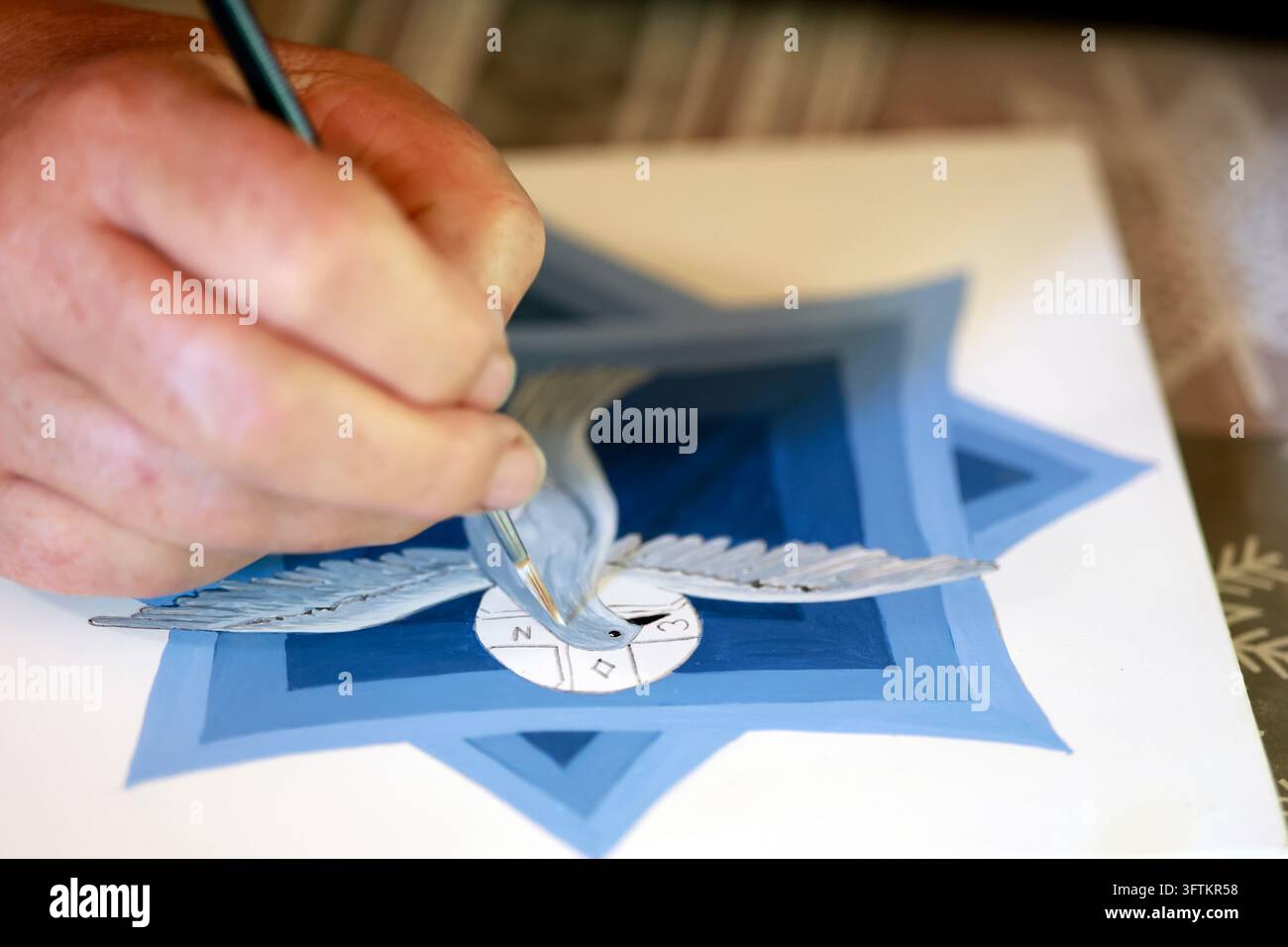 Un artigiano dipinge con cura l'immagine sacra di una colomba su un'icona religiosa utilizzando varie sfumature di blu. Foto Stock