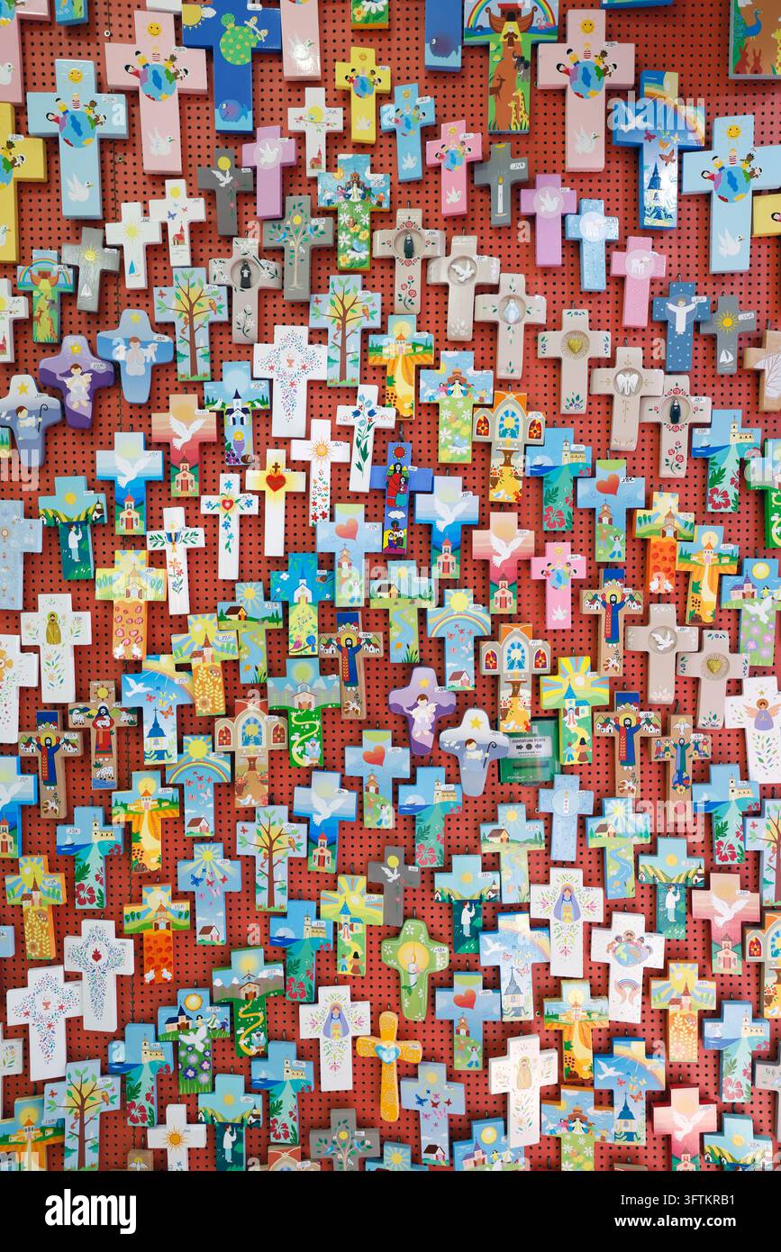 Molte piccole croci di legno dipinte con disegni colorati sono esposte sulla parete rossa di un negozio di souvenir religiosi. Lourdes, Francia. Foto Stock