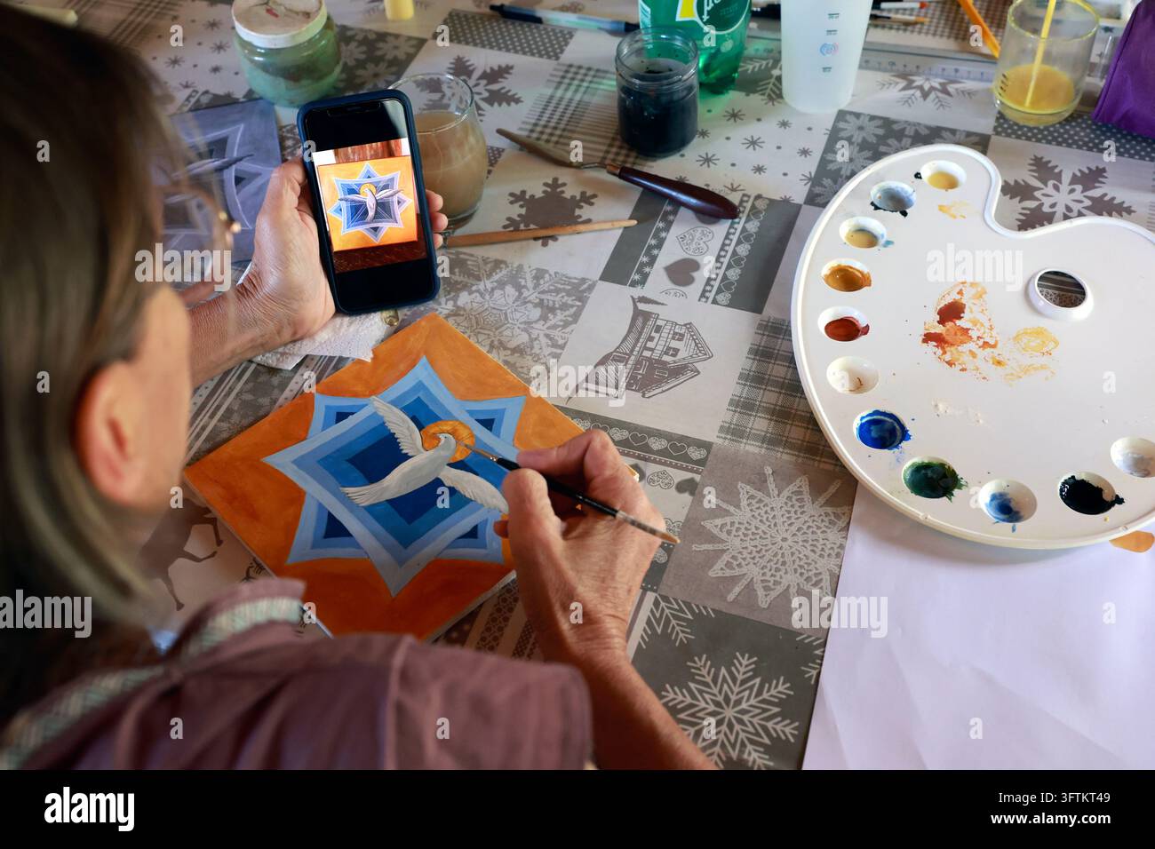 Un artista sta dipingendo delicatamente un'icona religiosa raffigurante una colomba mentre guarda un'immagine di riferimento visualizzata su un telefono. Foto Stock