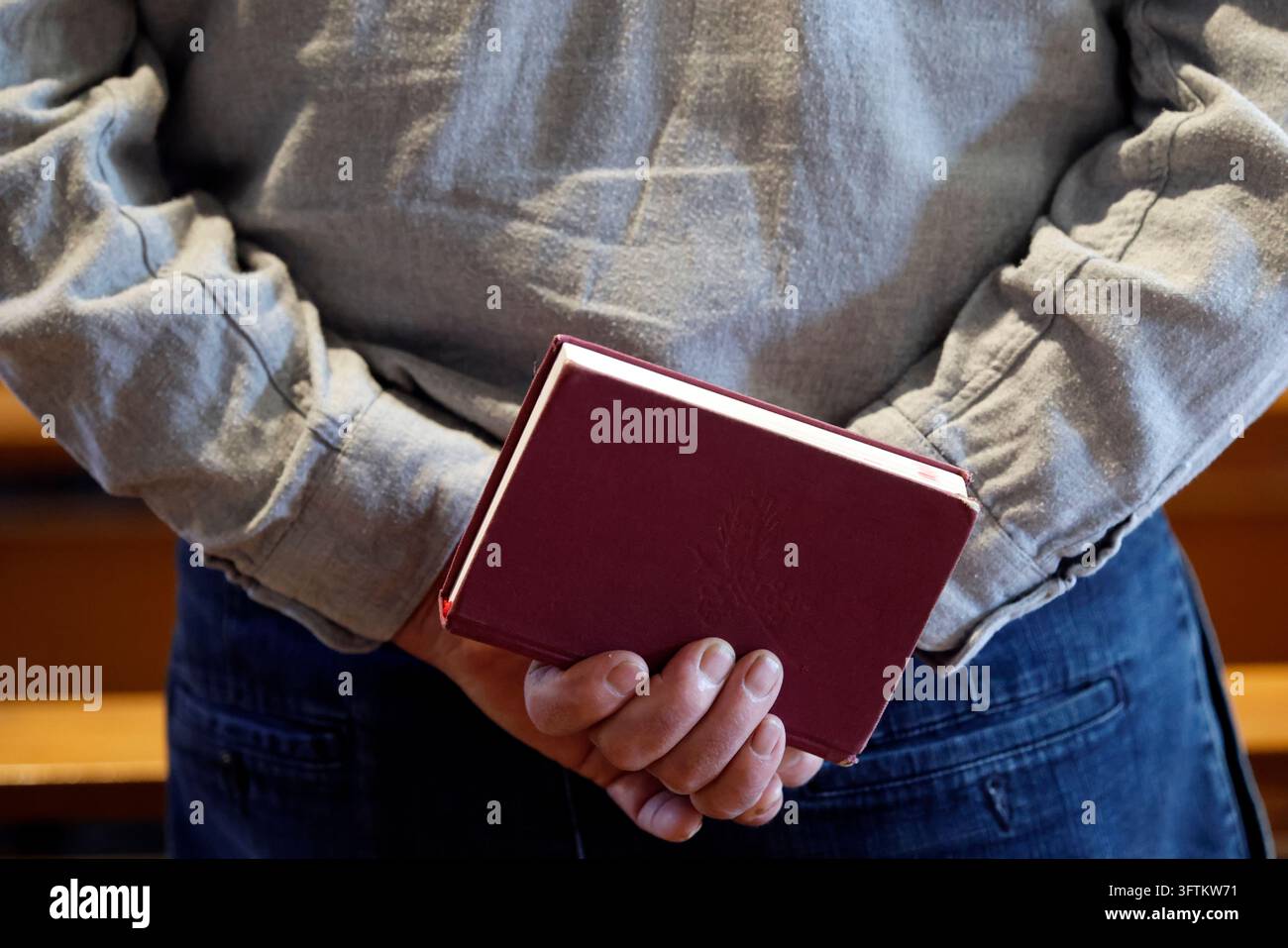 Messa cattolica. Un uomo con una camicia grigia tiene un libro di canti dietro la schiena. Foto Stock