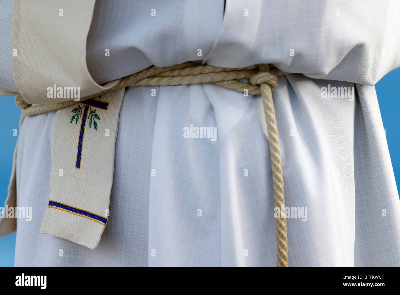 Un primo piano di un alb bianco di un prete, stretto in vita con una corda intrecciata, con una stola ricamata con una croce blu. Foto Stock
