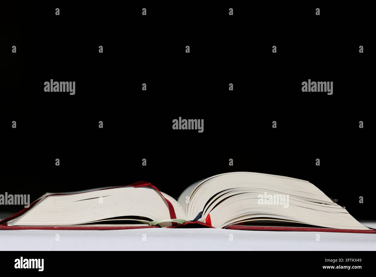 Un libro liturgico aperto poggia su una tovaglia bianca su uno sfondo nero semplice. Foto Stock