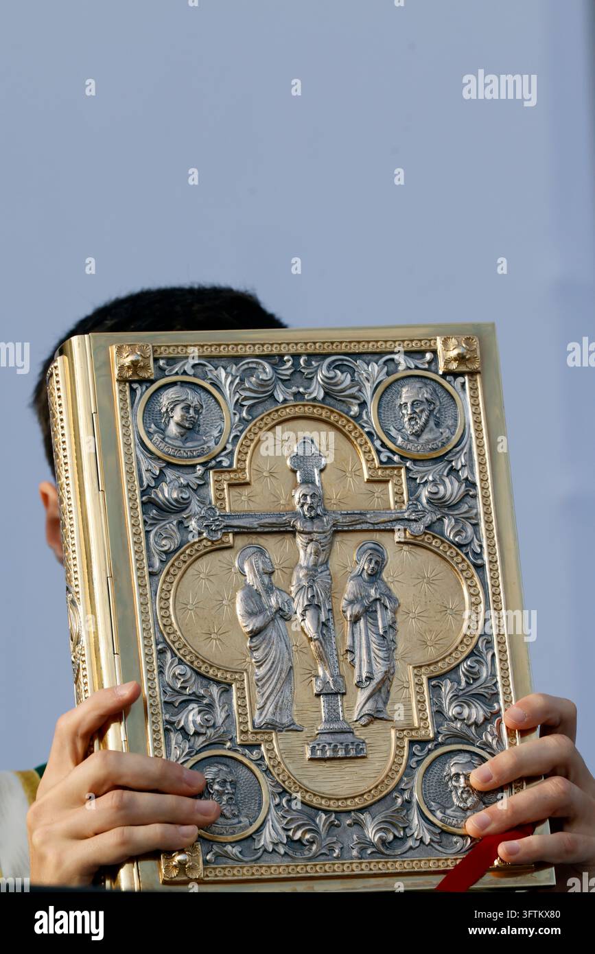 Un sacerdote tiene un libro evangelico riccamente adornato con metalli preziosi durante la Messa celebrata da Papa Leone XIV. Liturgia della Parola. Lourdes, Francia. Foto Stock