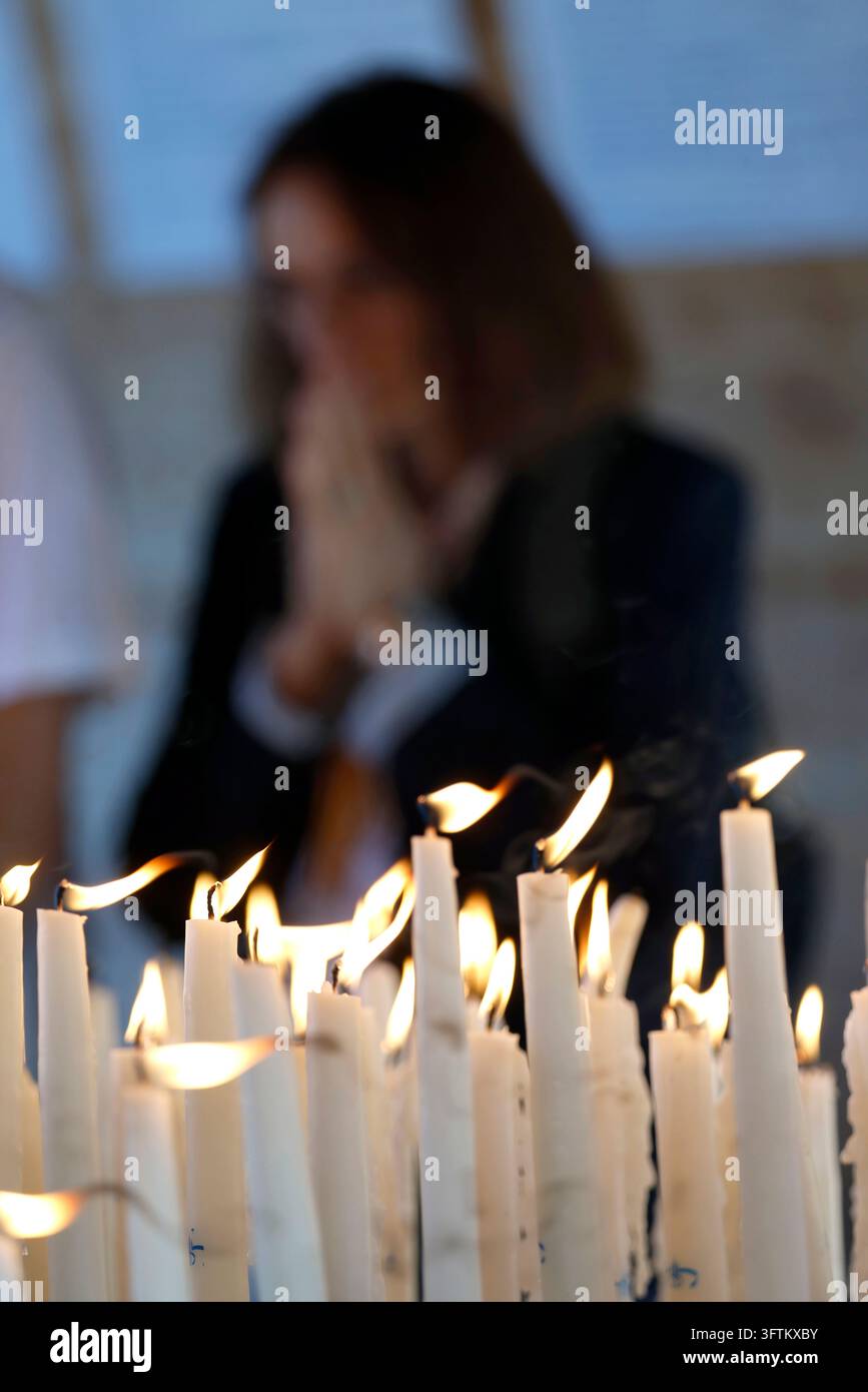 Candele accese proiettano una luce calda su una donna in preghiera. Lourdes, Francia. Foto Stock